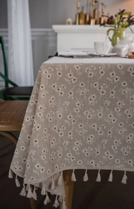 Detail of linen tablecloth with daisy floral embroidery and elegant tassel fringe border
