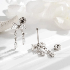 Silver bow stud earrings with zircon chains and screw backs on white surface
