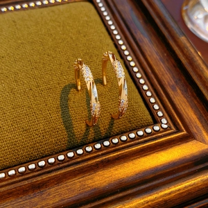 Close-up of 18K gold plated C-shaped twist earrings with zircons on velvet background