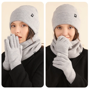 Detailed knit texture of light grey winter hat, scarf, and gloves set with logo patch
