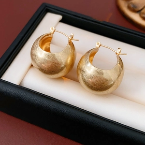 Close-up of golden spherical hoop earrings with brushed metallic finish in a black box