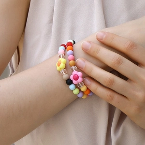 Colorful acrylic beaded bracelets with flower pendants on a female wrist in natural light