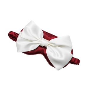 Burgundy silk satin sleep mask with white bow decoration and elastic strap on white background