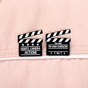Movie clapperboard enamel pins featuring motivational quotes on pink fabric background