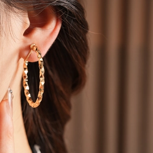 Close-up of gold geometric faceted C-shaped hoop earring on model showing glossy texture