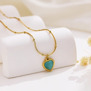 Golden snake chain necklace with turquoise heart pendant on a white geometric stand