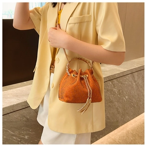 Detail of orange rhinestone bucket bag with metal handle and chain strap on model