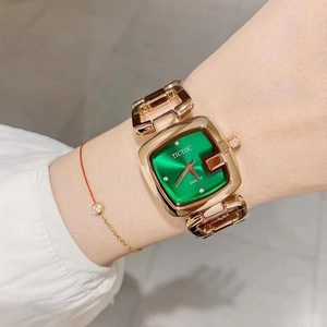 Close-up of elegant square green dial watch with gold hollow strap on woman's wrist