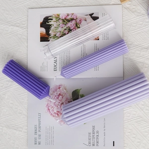 Grooved cylindrical pillar candle mold with finished purple striped candles on a magazine