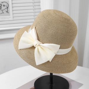Detail of the woven straw sun hat featuring a large white satin bow and elegant texture