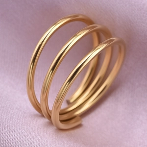 Macro view of a gold triple-layer coiled ring on soft pink fabric with soft lighting