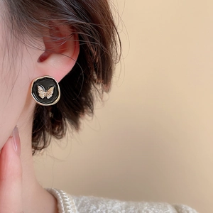 Détail de boucles d'oreilles vintage avec papillon doré et émail noir sur modèle