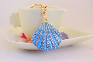 Close-up of blue enamel shell keychain with rhinestones next to a coffee cup