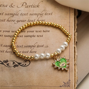 Detail of beaded bracelet with pearl accents and green enamel heart evil eye pendant