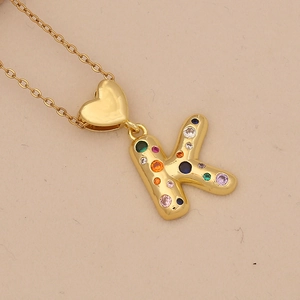 Macro shot of gold letter K pendant with colorful cubic zirconia and heart clasp detail
