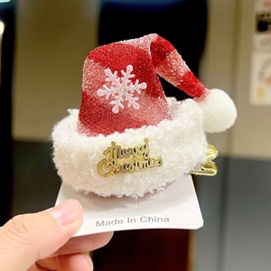 Detail of a Christmas hat hair clip with red plush fabric and Merry Christmas lettering