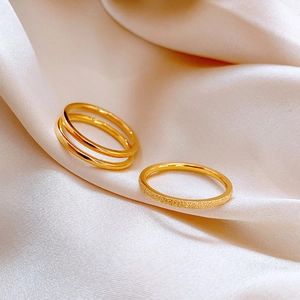 Detailed view of three stackable gold rings on silk, featuring frosted and double-loop designs