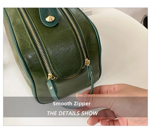 Détail de la double fermeture éclair dorée sur une trousse de toilette en cuir vert foncé