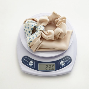 Close-up of floral scrunchie with bow tie on a scale showing 22.0g weight and soft fabric