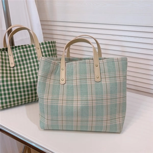 Detail of green plaid canvas tote bag showing leather handles with metal rivet reinforcement