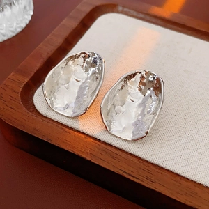Close-up of irregular silver earrings with hammered texture on a wooden tray