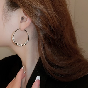 Close-up of model wearing large silver twisted hoop earrings with pavé rhinestones