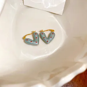 V-shaped heart earrings with light blue enamel and red polka dots in a white ceramic dish