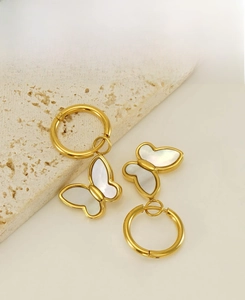 Détail de boucles d'oreilles créoles papillon dorées avec incrustation de nacre blanche