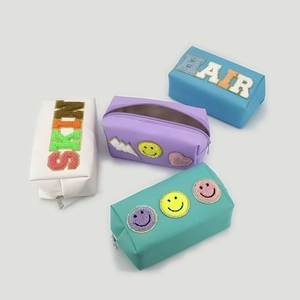 Detail view of colorful PU leather makeup bags with chenille letter patches and metal zippers