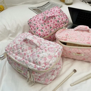 Three pink floral quilted makeup bags with handles displayed in a cozy lifestyle setting