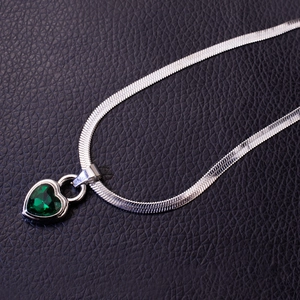 Silver snake chain necklace with a heart-shaped emerald green crystal pendant on black leather