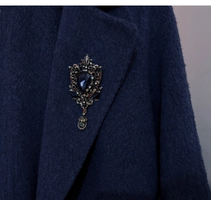 Detailed close-up of a vintage teardrop brooch with blue rhinestones on a coat lapel
