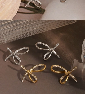 Macro detail of bow-shaped stud earrings with inlaid zircon in gold and silver finish