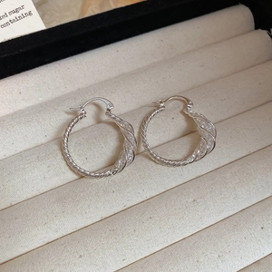 Close-up of silver twisted hoop earrings on a textured jewelry tray showing metal texture
