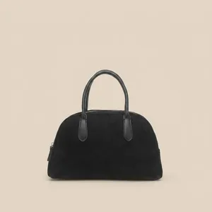 Detail of minimalist black faux suede bowling bag with leather handles and metal zip closure