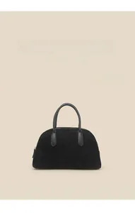 Detail of minimalist black faux suede bowling bag with leather handles and metal zip closure