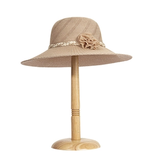 Macro detail of breathable wide-brim straw hat with elegant fabric flower on a wooden stand