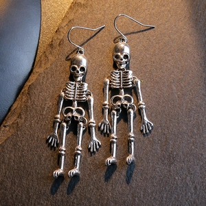 Silver skull drop earrings with articulated limbs and fishhooks on dark textured stone