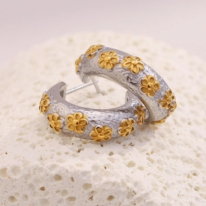 Macro detail of two-tone C-shape earrings with gold flower accents on sandblasted metal