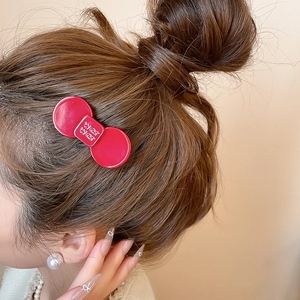 Detail shot of a bright red resin bow hair clip with embossed lettering on dark hair