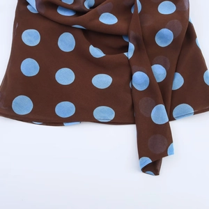 Detailed macro view of coffee chiffon fabric with blue polka dots and neat hemline finish