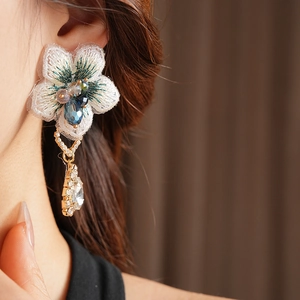 Gros plan sur des boucles d'oreilles fleurs brodées asymétriques avec pendentifs cristal