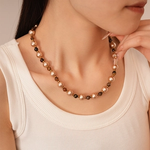 Close-up of champagne pearl and tiger eye stone necklace on model wearing white vest