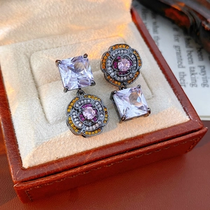 Macro shot of asymmetric vintage earrings with flower charms and square zircon stones