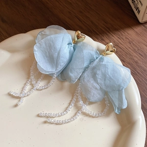 Close-up of blue tulle flower earrings with gold heart studs and bead tassels