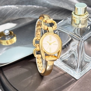 Close-up of a luxury gold bangle watch with a Roman numeral dial on a soft fabric