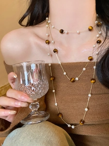 Detail of layered necklace with tiger eye beads and pearls over a brown sweater