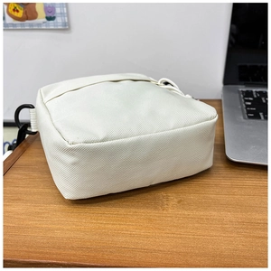 Close-up of durable cream canvas crossbody bag with adjustable black buckle on wood desk