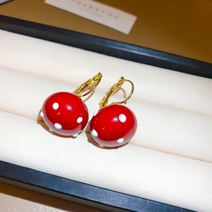 Detail of gold-plated red mushroom earrings with white polka dots in a velvet box
