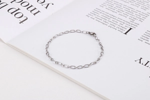 Detailed view of silver cable chain bracelet with lobster clasp on vintage magazine